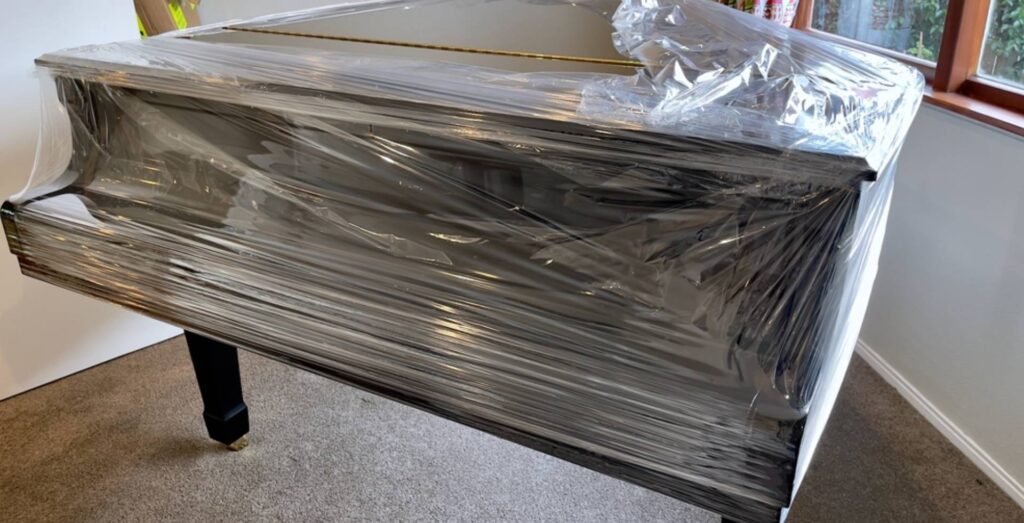 Glossy black grand piano partially covered in plastic wrap in preparation for removal by furniture moving company