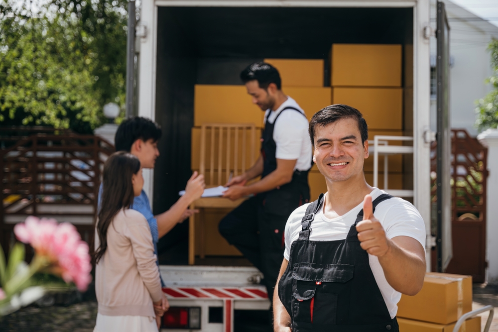 A smiling mover captured in a portrait unloads boxes into a new home from a truck